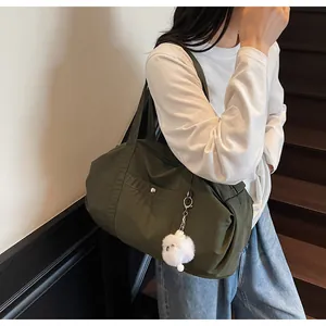 Close-up of olive green nylon tote bag with silver buckle and white plush ball charm