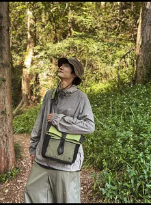 Outdoor urban crossbody bag with brown bucket hat and grey jacket in nature setting
