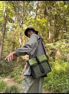 Detail view of a green textured outdoor messenger bag with black buckles on a model