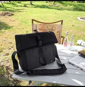 Macro view of black crossbody messenger bag with buckle closure on a camping table