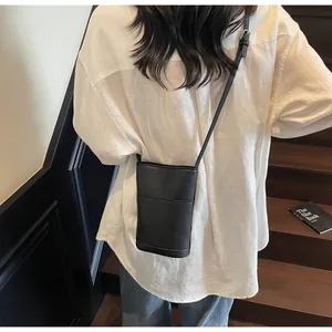 Dettaglio di una borsa a secchiello in pelle nera con trama a grana indossata da una modella