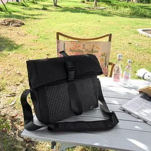 Black outdoor messenger bag with grid pattern on a white camping table in nature