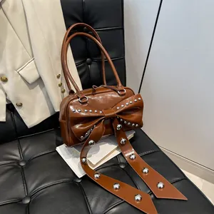 Bruine vintage handtas met grote strik en zilveren klinknagels op een leren bank