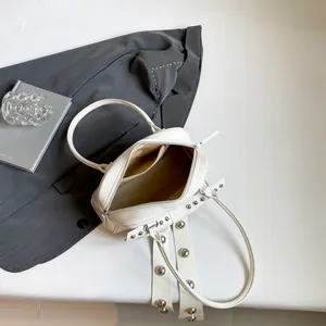 Witte handtas met zilveren klinknagels en dubbele handgrepen op een grijze blazer achtergrond