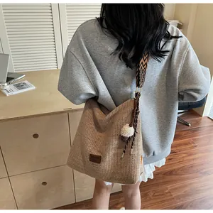Dettaglio borsa tote in paglia con tracolla ricamata e ciondolo decorativo