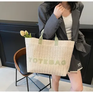 Détail d'un sac cabas en paille tressée avec anses vertes et broderie TOTEBAG