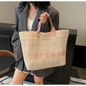 Détail du sac cabas en paille tressée avec anses en cuir rose et logo brodé décoratif