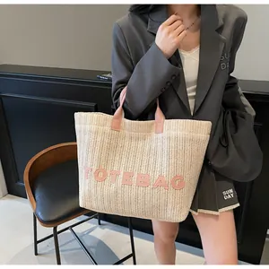 Détail d'un grand sac cabas en paille avec anses en cuir rose et lettres roses en relief