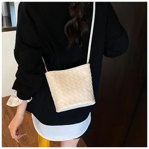 Dettaglio di una borsa a secchiello in pelle intrecciata beige con trama a croce e tracolla