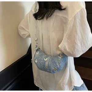 Dettaglio borsa a mezzaluna in denim blu con farfalle d'argento e tracolla a corda
