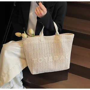 Détail du sac cabas tissé crème avec lettrage TOTEBAG sur un escalier en bois