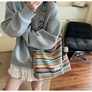 Dettaglio di borsa tote in paglia colorata con ciondolo pompon e tracolla larga a motivi