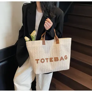 Détail d'un sac cabas en paille tressée avec anses en cuir marron et étiquette TOTEBAG