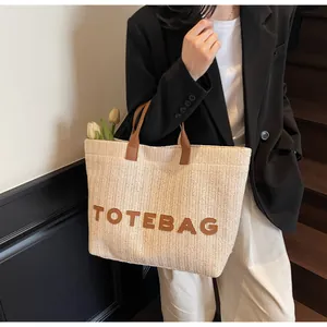 Détail du sac cabas en paille tissée avec anses en cuir brun et écusson 'TOTEBAG'