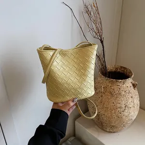 Borsa a secchiello intrecciata giallo chiaro minimalista con tracolla su sfondo naturale