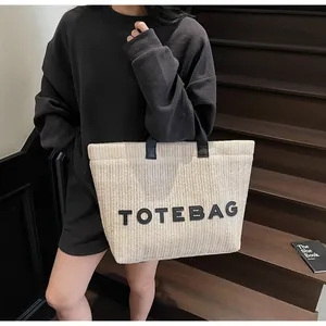 Gros plan détaillé d'un sac cabas en paille avec lettrage TOTEBAG noir et anses en cuir