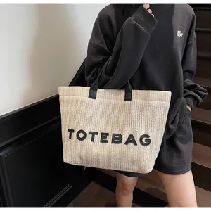 Détail macro de la texture tissée beige et lettrage TOTEBAG en cuir noir sur le sac