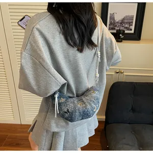 Borsa a mezzaluna in denim blu con farfalla metallica indossata da una modella in casa