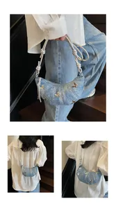 Dettaglio borsa croissant in denim blu con farfalle dorate e tracolla argento annodata