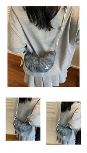 Dettaglio borsa a mezzaluna in denim blu con farfalle metalliche e tracolla a corda