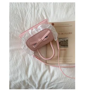 Dettaglio borsa in ecopelle rosa con bordo in pizzo bianco e fiocco su tessuto bianco