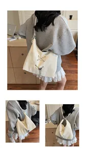 Detail of cream tote bag with silver cross-straps, metallic bows and pearl pendant charms