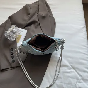 Borsa a mezzaluna in denim azzurro con farfalle argentate su sfondo di letto bianco