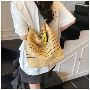 Dettaglio borsa tote in paglia intrecciata con strisce nere e perline colorate sul manico