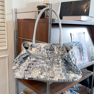 Dettaglio di una borsa tote in paillettes argento con tracolla lunga su supporto metallico