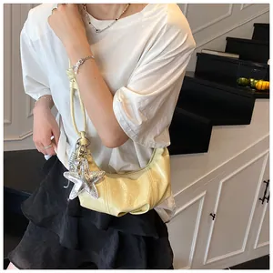 Detail of light yellow crescent bag with shiny star charm and metallic chain strap