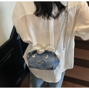 Detail of blue denim bucket bag with silver butterfly charms and elegant chain strap