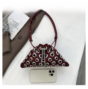Detail view of burgundy rivet bucket bag with silver eyelets and phone for size comparison