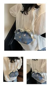 Detail of blue denim cloud bucket bag with silver butterfly accents and chain strap