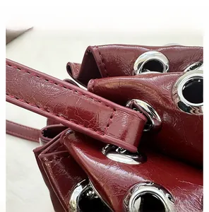 Detailed close-up of fine stitching and silver eyelets on a burgundy bucket bag