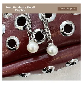Macro detail of red patent leather bag with silver eyelets and a pearl pendant charm