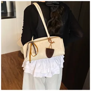Détail du sac à bandoulière en cuir crème avec breloque vintage marron sur le modèle