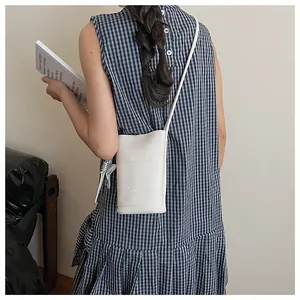 Detail of a beige lychee leather mini crossbody phone bag on a gingham dress