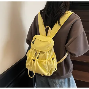 Side view of bright yellow nylon drawstring backpack worn on shoulders against wooden stairs