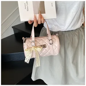 Gros plan d'un sac cylindrique matelassé rose avec fermoir doré et nœud en dentelle