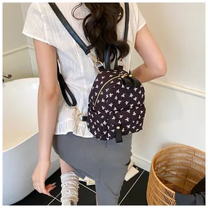 Close-up of stylish black quilted mini backpack with white bow patterns worn by a model