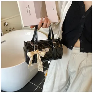 Détail d'un sac cylindrique matelassé noir avec nœud en dentelle et fermoir argenté