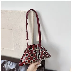 Close-up of deep red glossy leather bucket bag with silver eyelets and pearl charm detail