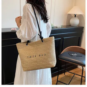 Detail of a beige woven straw tote bag with black strap and printed TOTE BAG text