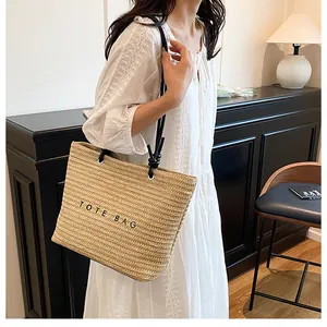 Detail of a large straw tote bag with black TOTE BAG text and shoulder straps on a model
