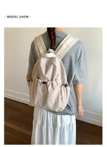 Detail of cream pleated backpack featuring side drawstring pockets and padded straps