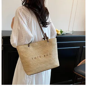 Detail view of woven straw tote bag featuring brown leather straps and Tote Bag embroidery