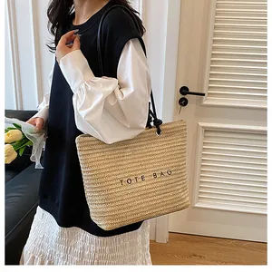 Detail of straw tote bag with black shoulder straps and TOTE BAG lettering detail