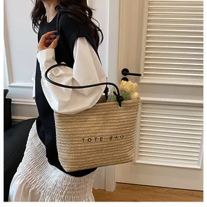 Straw tote bag styled on model with black handles and elegant black lettering