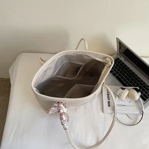 Minimalist off-white leather tote bag with interior pockets and decorative silk scarf detail
