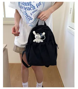 Detail of black canvas backpack with drawstring pocket and cute plush bear accessory